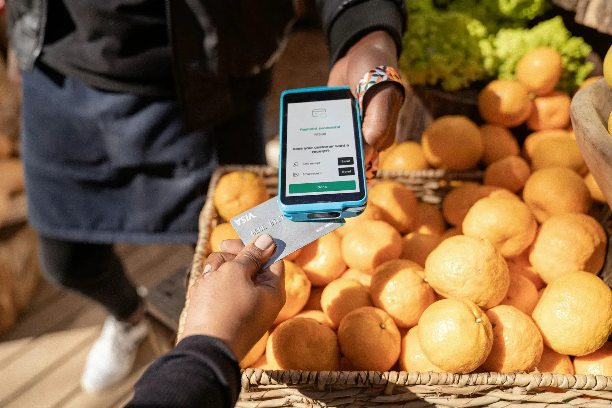 Client payant par carte sur un terminal de paiement mobile devant un étal d'oranges