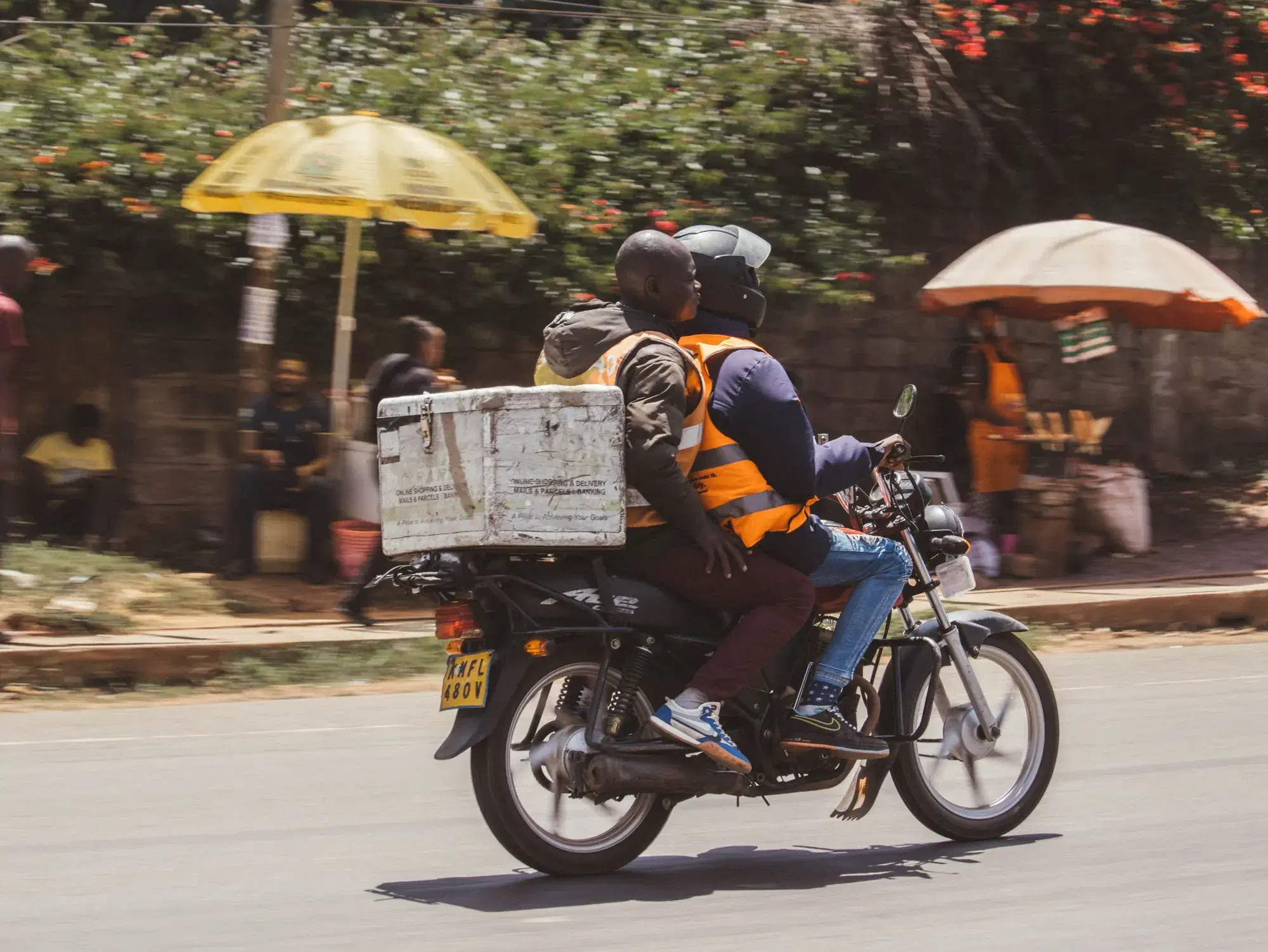 Livreur et passager transportant un coffre à colis à moto dans une rue de Nairobi